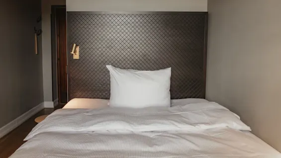 Ett mysigt hotellrum på Home Hotel Grand, Helsingborg, med en bekväm säng med krispiga vita lakan och en stilren sänggavel.