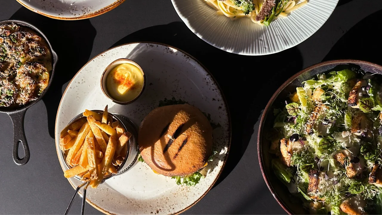A delicious meal featuring a burger, fries, pasta, and a fresh salad, beautifully arranged on a table.