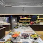 Buffet table displaying assorted salads, fruits, and pastries; situated in a modern dining area with wooden floors and decorative shelves, under bright lighting.
