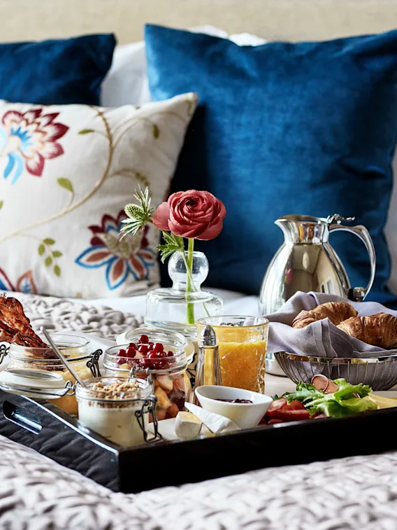 Herkullinen aamiaistarjotin croissanteilla, mehulla, hedelmillä ja pekonilla sängyllä, viitaten rentouttavaan aamuun.