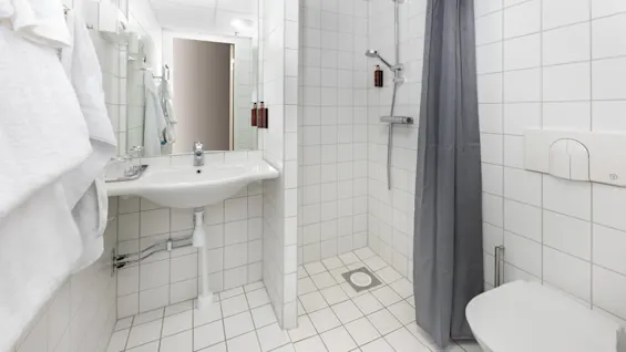 A clean, white-tiled bathroom featuring a sink, shower, and toilet in a compact space.