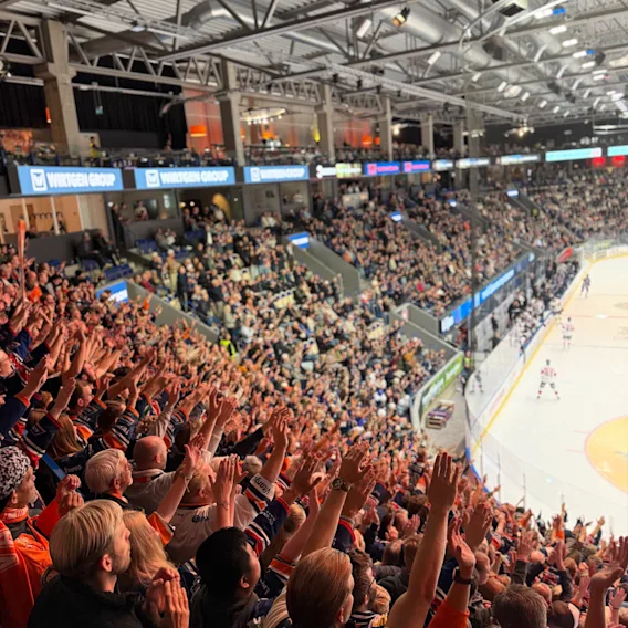 Hejande publik som jublar och stracker upp handerna pa en fullsatt ishockeymatch i en arena