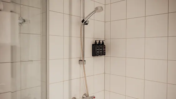 En modern dusch med vita kaklade väggar, ett duschhuvud och väggmonterade toalettartiklar, redo att användas.