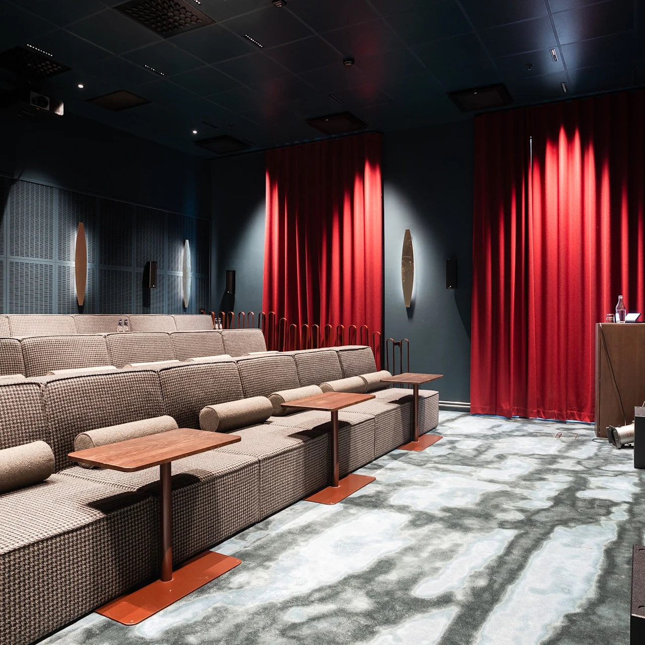 A cozy private cinema with tiered seating, individual tables, and a large screen, ready for a movie experience.