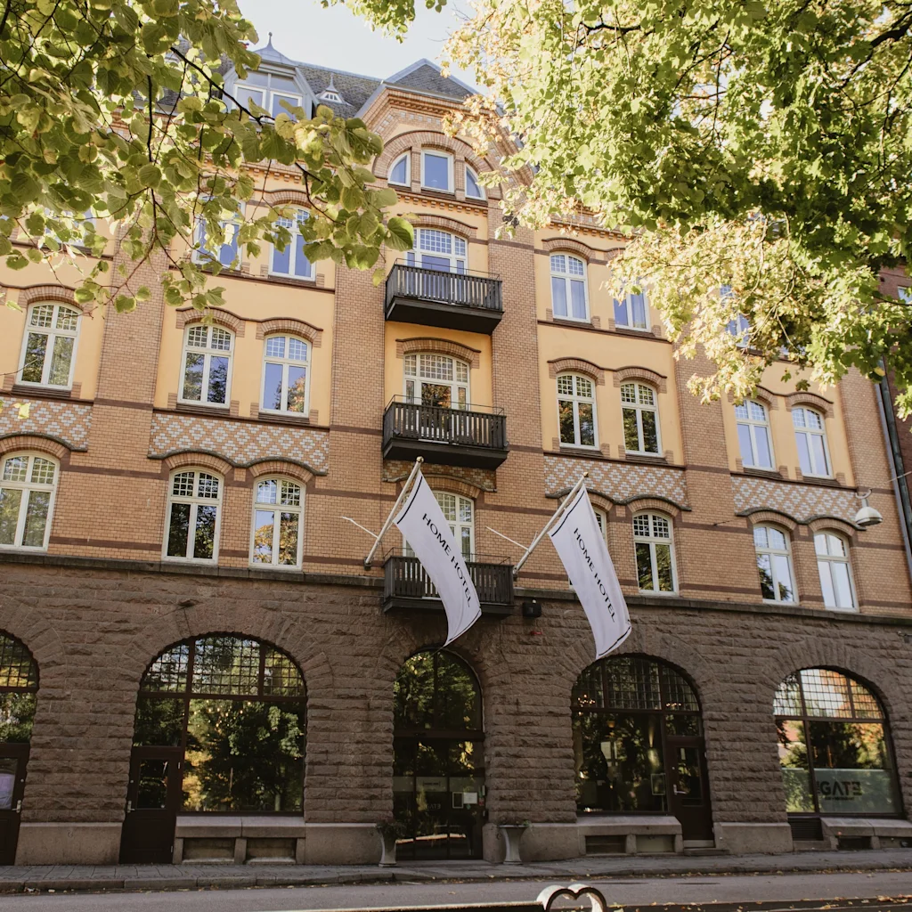 Home Hotel Norre Park in Halmstad, a charming building with flags, framed by green trees on a sunny day.