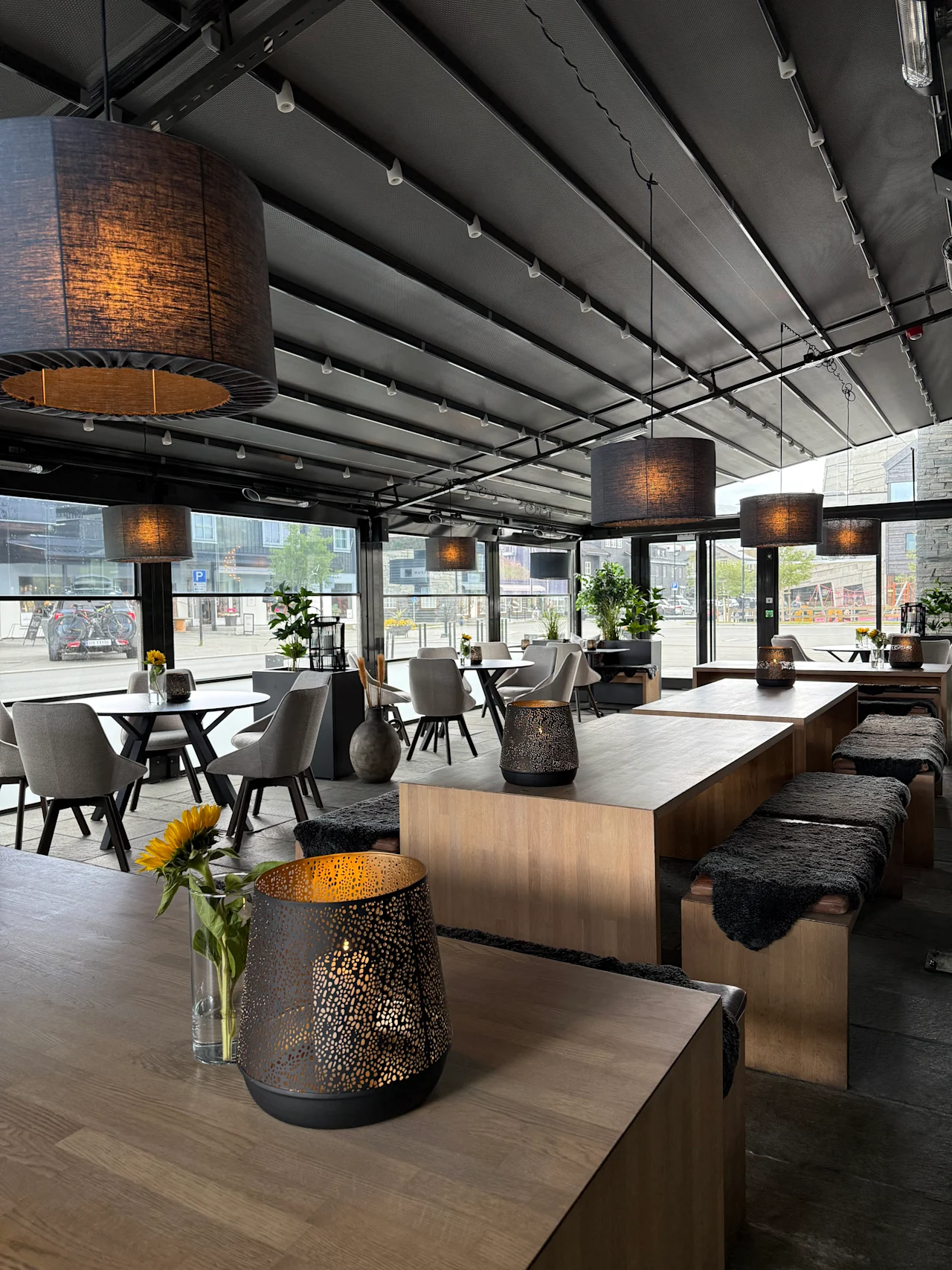 Modern covered outdoor patio with wooden tables, cozy hanging lamps, and decorative lanterns.