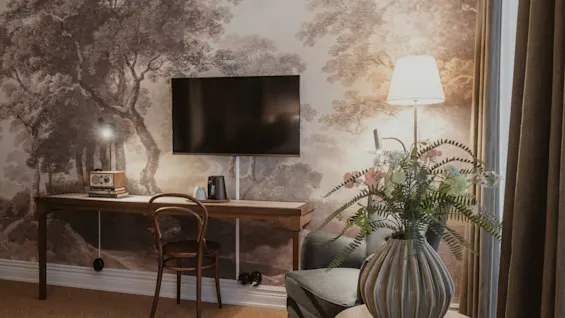 Home Hotel Baltzar - Superior Room. A cozy room with a desk, TV, and armchair, featuring a nature-inspired wall mural.