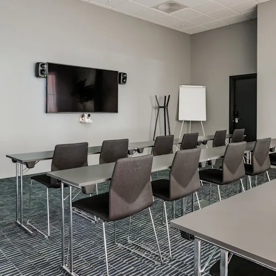 Classroom setup with rows of chairs facing a wall-mounted TV. Next to it, a flipchart stand and a plant enhance the room's modern, professional atmosphere. 