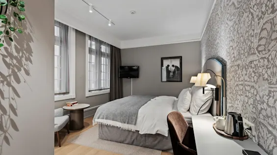 A stylish hotel room with a large bed, a functional workspace, and a relaxing corner, designed for comfort and productivity.