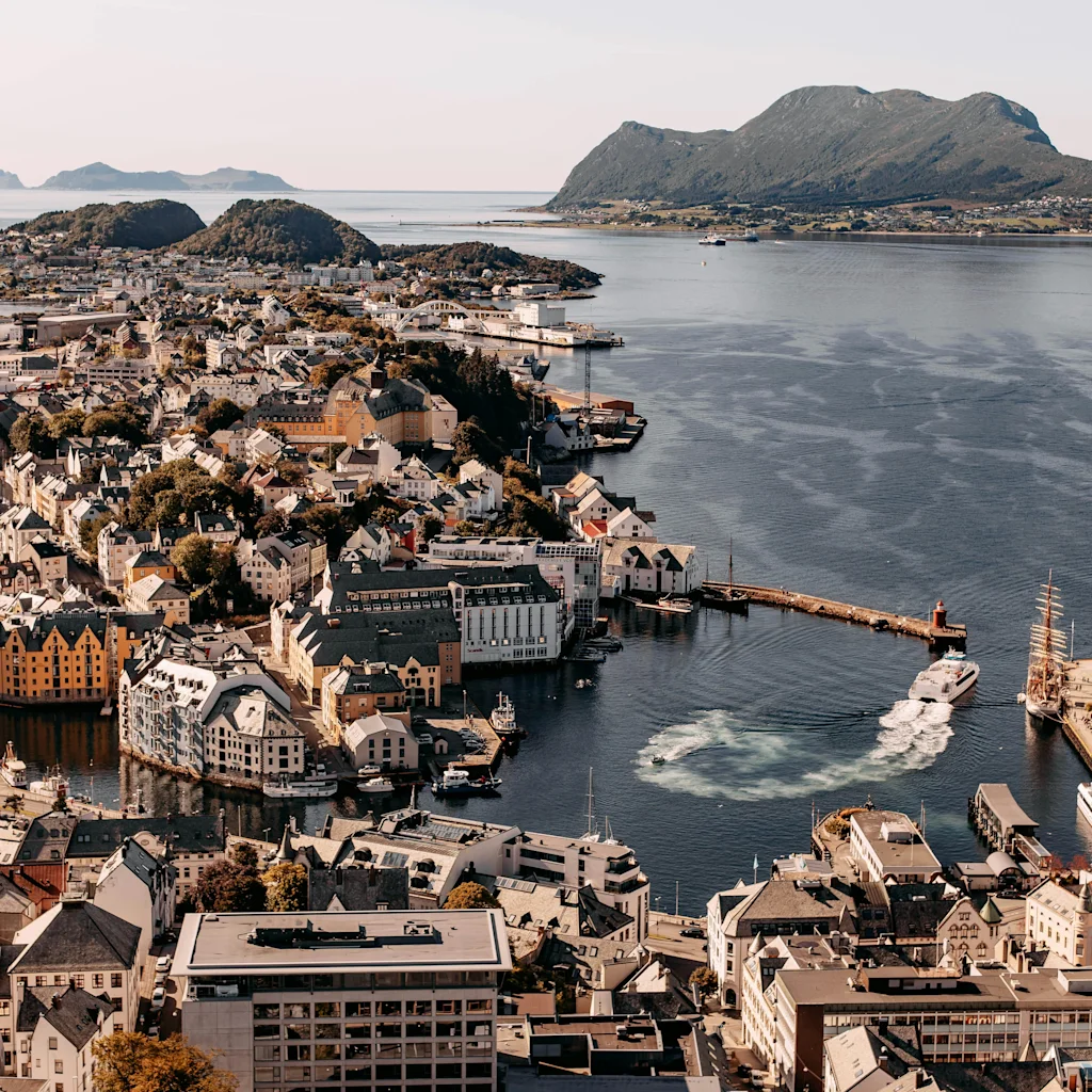 An aerial view of a picturesque coastal town with colorful buildings nestled along a fjord, surrounded by mountains and boats.