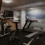 Ett välutrustat gym på Home Hotel Grand, Helsingborg, med olika träningsmaskiner och en naturskön väggmålning av en strandpromenad.