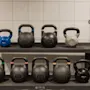Et stativ med ulike kettlebells og en vektstang i et treningsstudio. Vektene inkluderer 8KG, 12KG, 16KG, 20KG og 24KG.