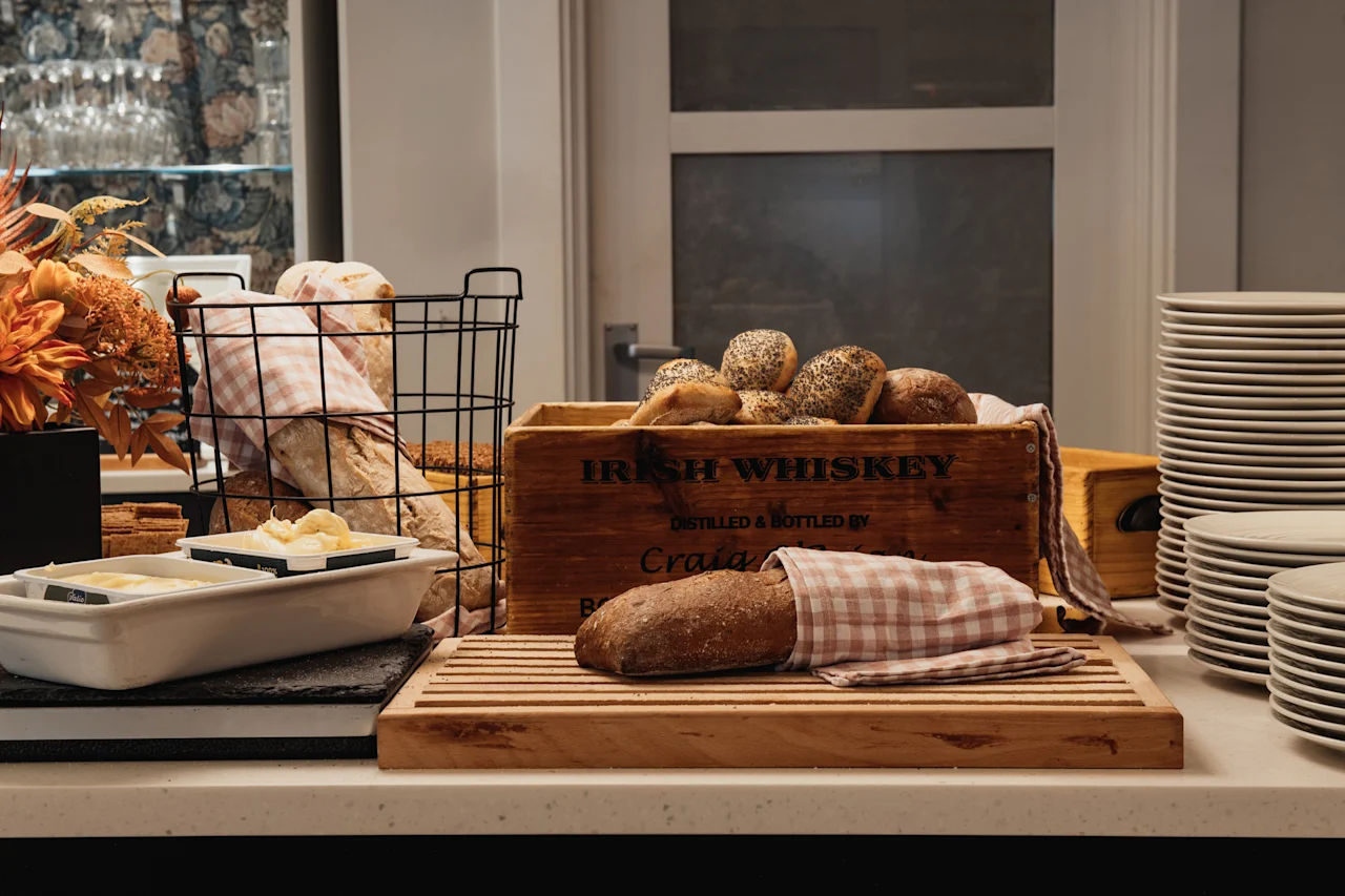 En selvbetjeningsmorgenmadsstation med et udvalg af frisk brød, smør og pænt stablede tallerkener.
