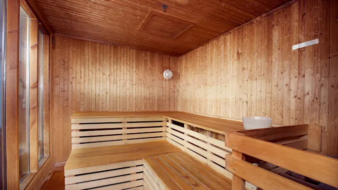 Wooden sauna interior, with benches and a water bucket, evoking tranquility. The thermometer and hygrometer indicate temperature and humidity control.