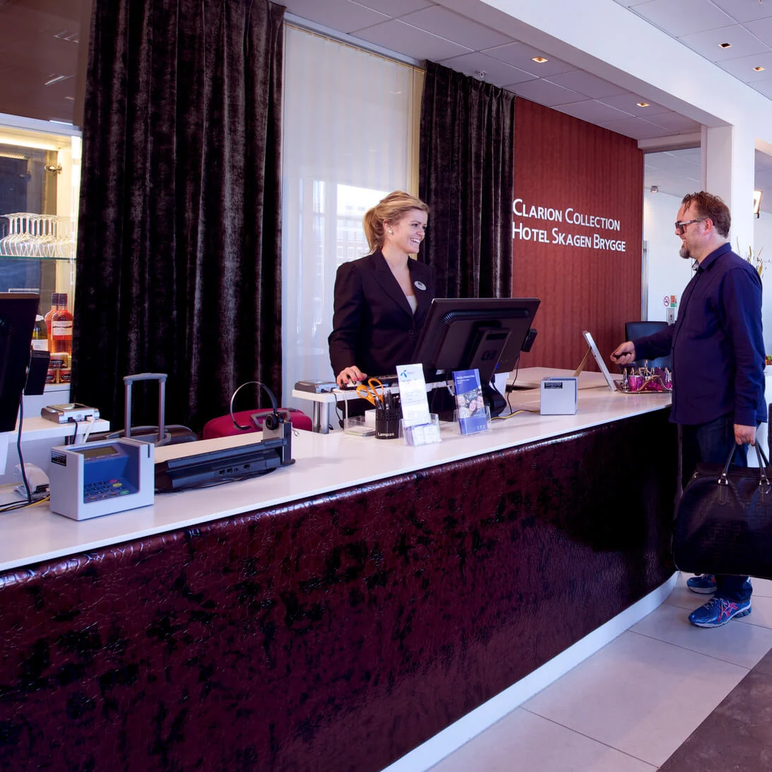 A hotel receptionist assists a guest; modern lobby with comfortable seating; warm tones.