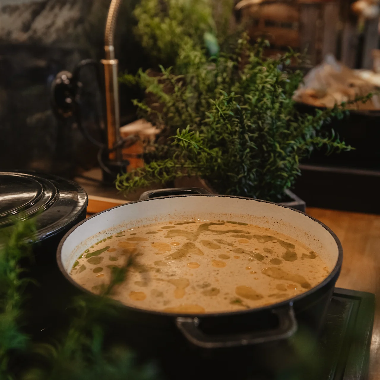 Dampende gryde på komfuret simrer med rig suppe; omgivet af frodigt grønt i et rustikt køkken.
