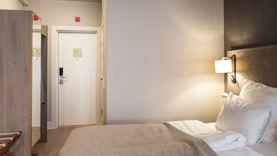 A welcoming hotel room at Home Hotel Grand Bodø with a comfortable bed, bedside lamp, and a wardrobe, ready for a relaxing stay.