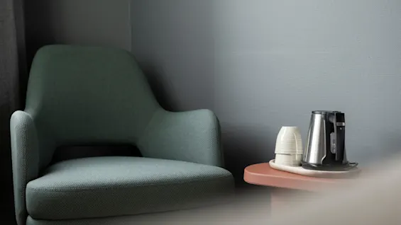 A cozy corner with a comfortable armchair and a small table holding a kettle and cups, inviting a moment of relaxation.
