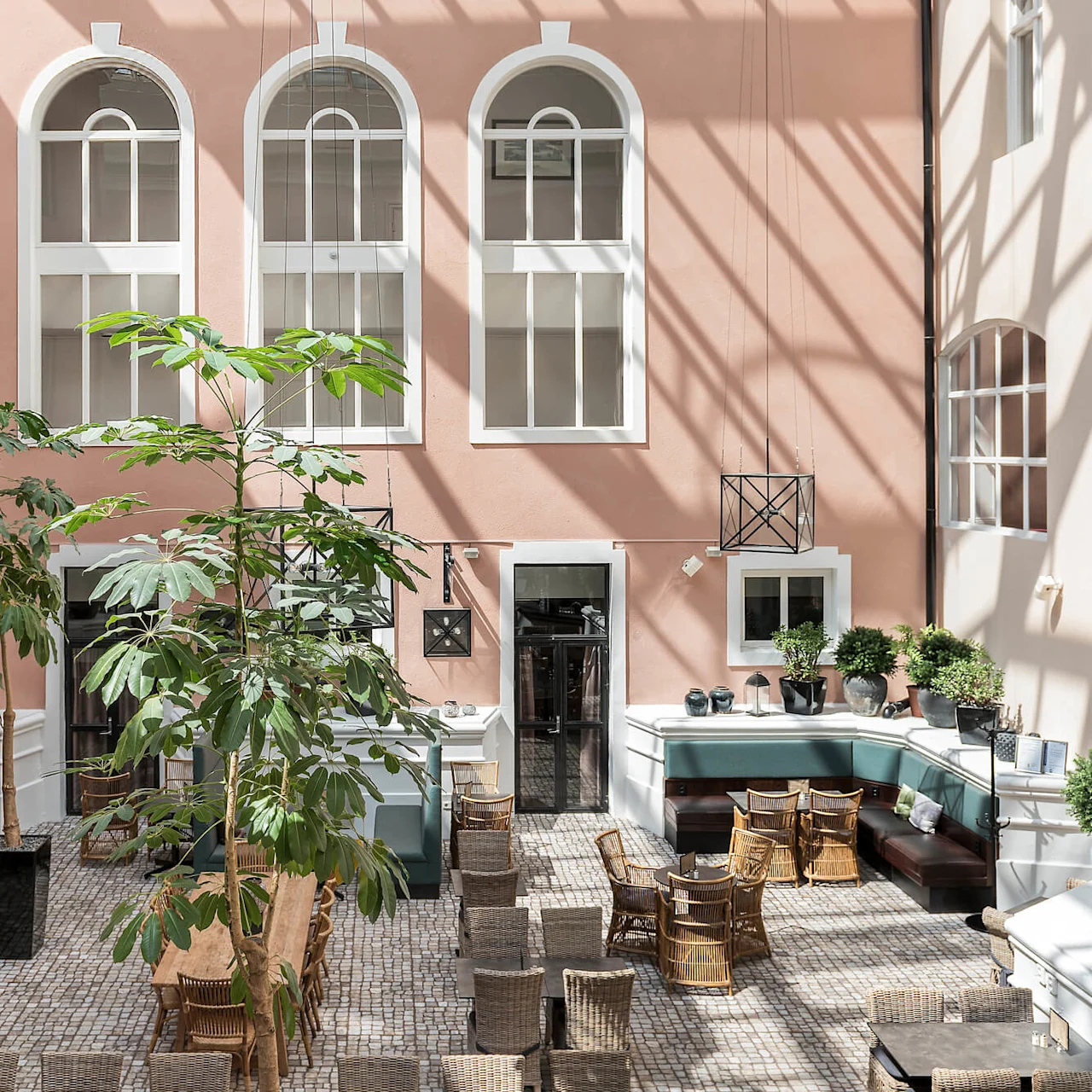 Ett solbelyst atrium med bord, stolar och grönska; en avslappnad matsalsmiljö inomhus.
