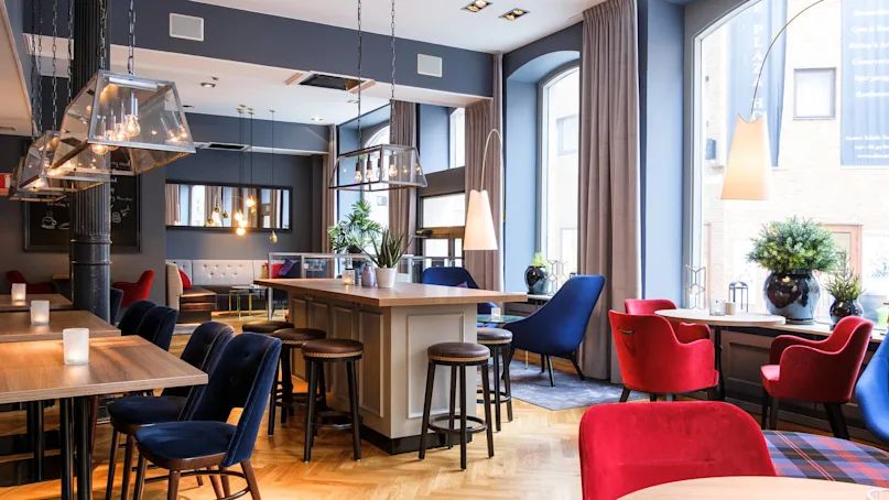 An elegant lounge with mixed seating including red and blue chairs, under stylish pendant lighting, reflecting a modern, cozy interior.