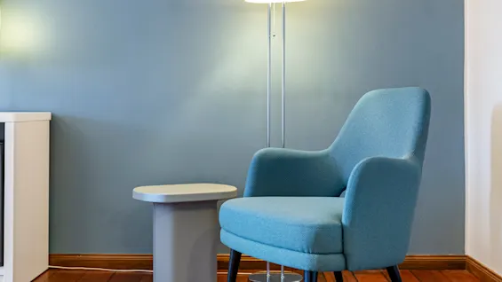 A blue armchair beside a white floor lamp, with a small table, in a room with blue walls and wooden floor.