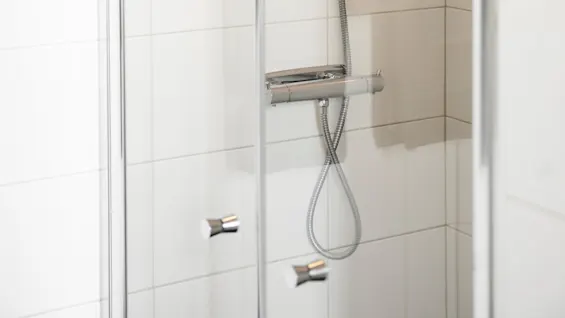 En modern dusch med en handhållen duschslang är monterad på en kaklad vägg i ett duschutrymme av glas.