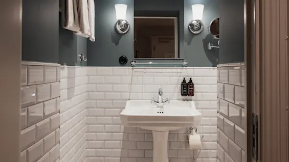 Home Hotel Baltzar - Compact Cabin. A stylish bathroom featuring a pedestal sink, mirror, and classic white subway tiles.