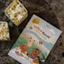 A children's activity booklet titled "Lollo & Bernie Activity Book" lies on a marble table beside two small open boxes of popcorn. The booklet features colorful illustrations of animals.