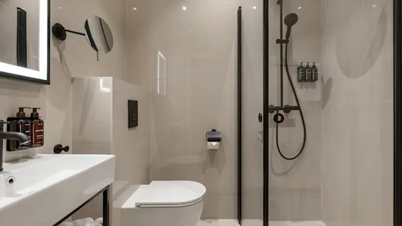 Et moderne badeværelse med en elegant håndvask, toilet og en bruser med mørke armaturer.