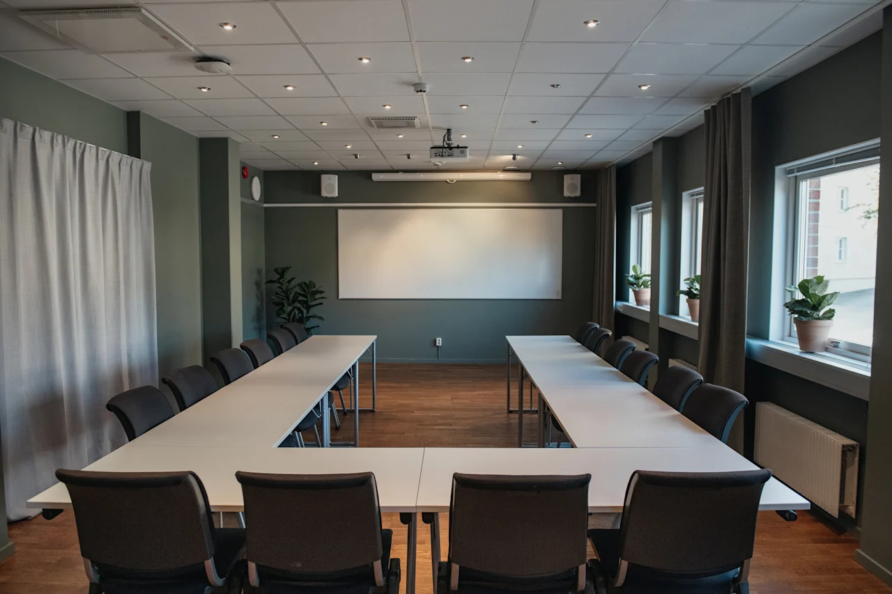 Ett modernt konferensrum med U-formad bordsuppställning, en stor whiteboard och en projektor, redo för ett möte eller presentation.