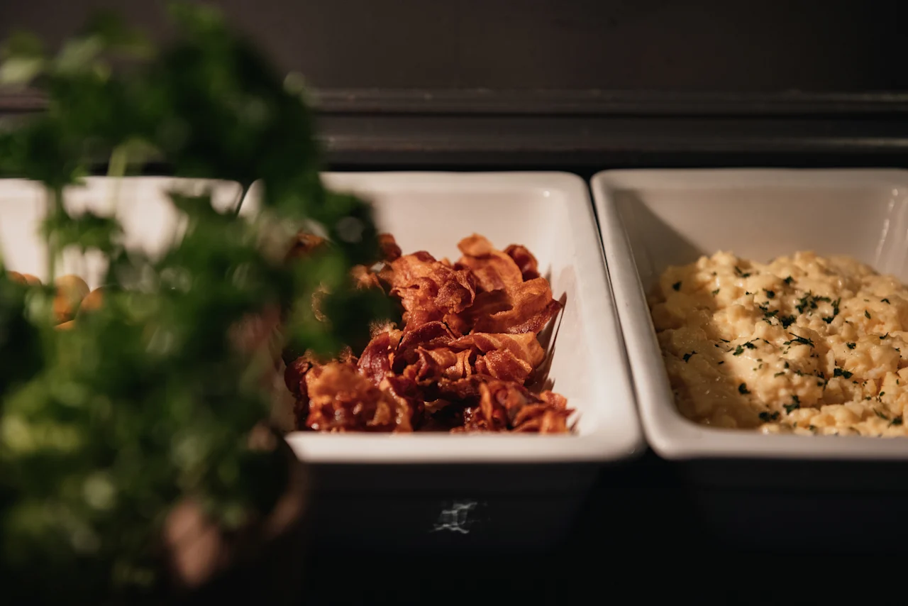 Home Hotel Kung Oscar: A delicious breakfast spread featuring crispy bacon and fluffy scrambled eggs with herbs.