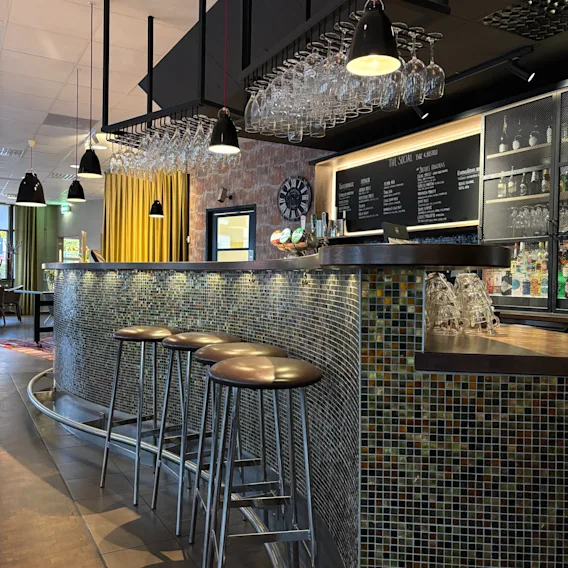 En modern bar med mosaikklädd disk, barstolar och hängande glas. En menybräda läser THE SOCIAL BAR BISTRO.