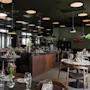 Et stilfullt og romslig restaurantinteriør med mange bord dekket for bespisning, med moderne innredning, store vinduer og varm belysning.