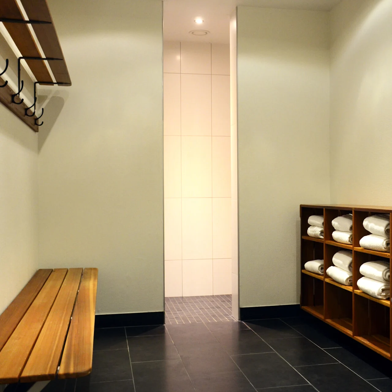Wooden bench and coat rack in a tranquil spa locker room with neatly arranged towels on shelves.
