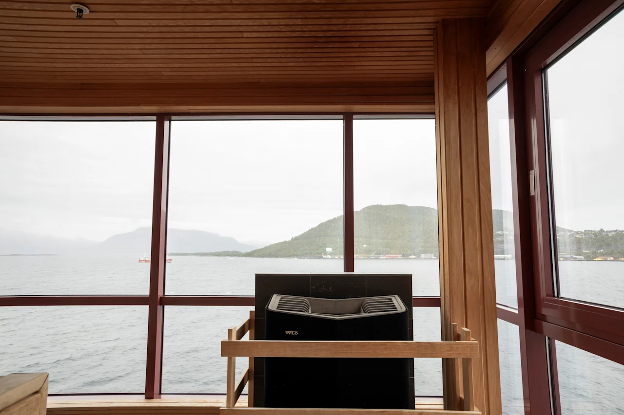 Sauna, josta on panoraamanäkymä järvelle ja vuorille, moderni kiuas ja puinen sisustus.