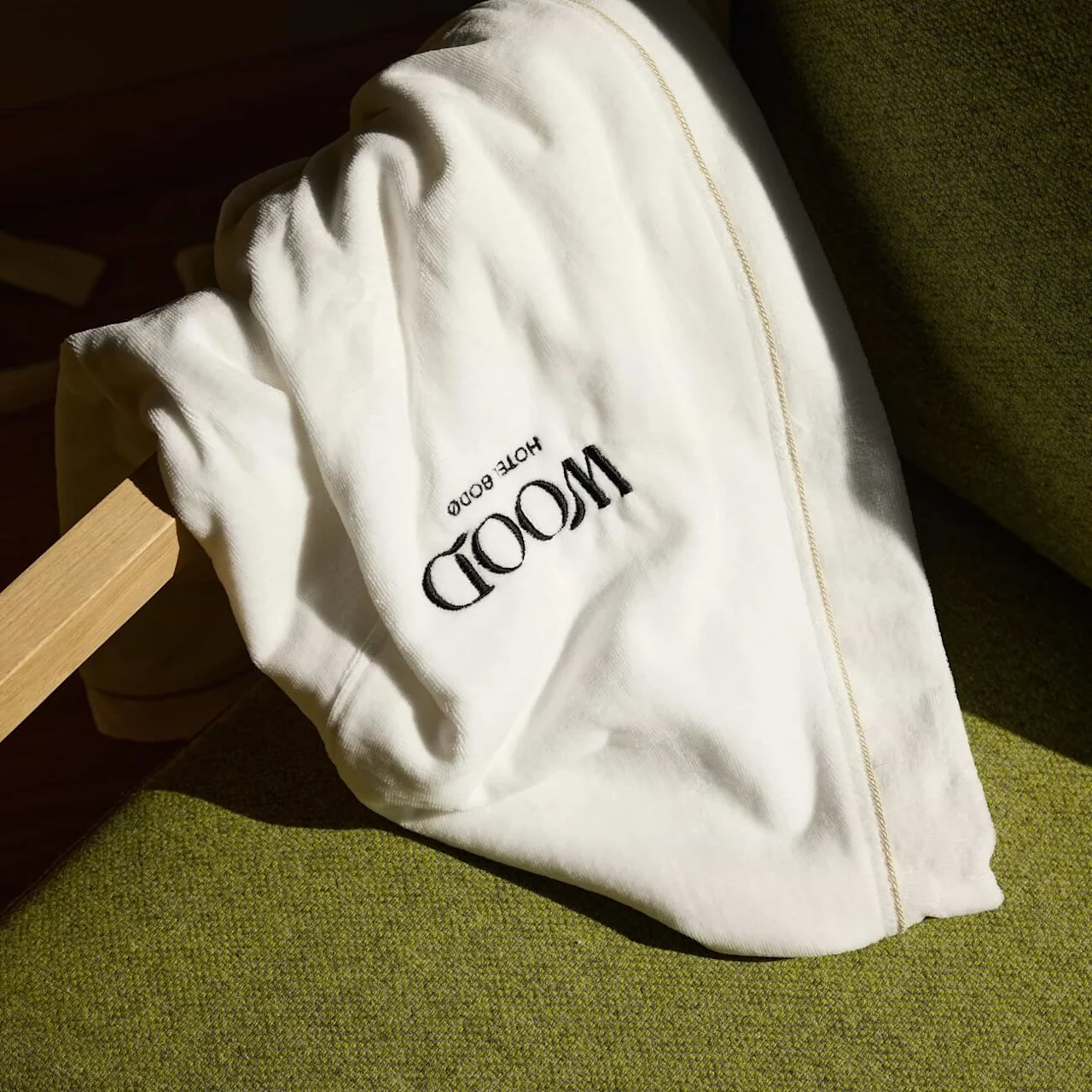 A white towel drapes over a green chair; sunlight casts shadows. Text on the towel reads "MOOD HOTEL GOOD."