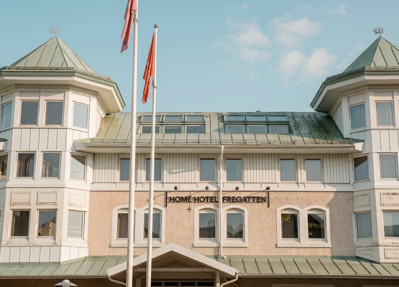 Byggnadens exteriör med en skylt som lyder HOME HOTEL och två flaggor som vajar framför under en klar himmel.