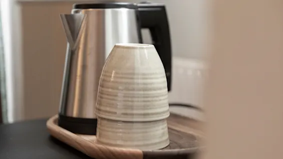 Ruostumattomasta teräksestä valmistettu vedenkeitin ja kaksi keraamista kuppia puutarjottimella, valmiina lämpimälle juomalle Home Hotel Victoriassa.