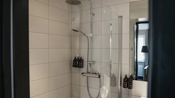 Virkistävä suihkukokemus odottaa tässä modernissa kylpyhuoneessa, jossa on valkoiset laatat, sadesuihku ja kätevät annostelijat.