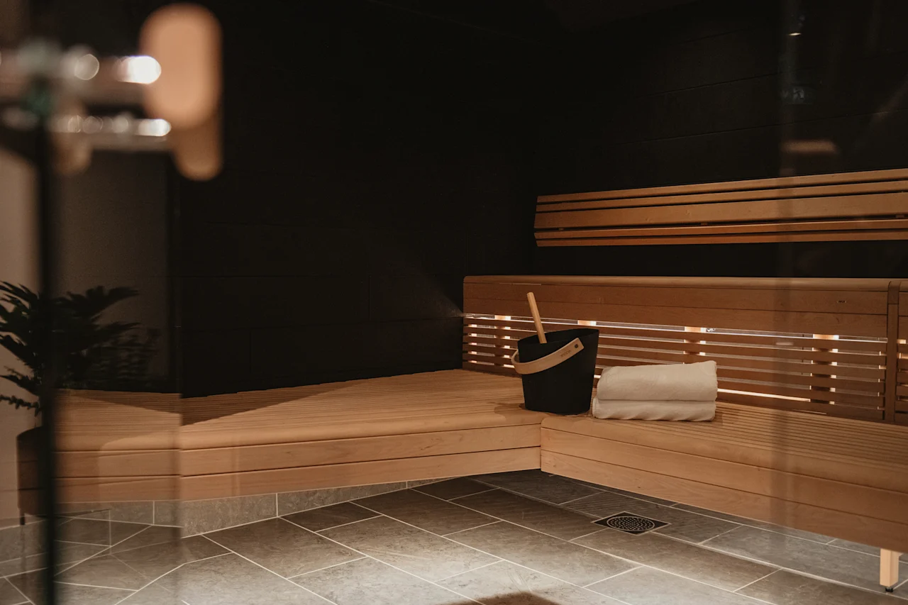 Et koselig badstuinteriør med trebenker, en bøtte og brettede håndklær, som inviterer til avslapning og varme.