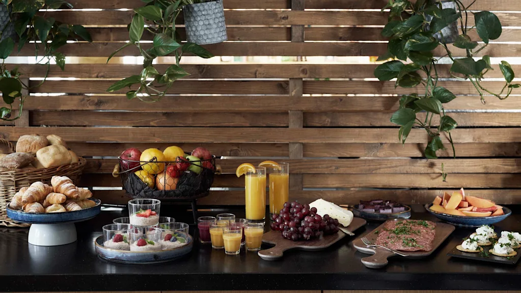 En färgstark buffé med färsk frukt, bakverk, juicer och salta rätter, uppdukad mot en varm träbakgrund.