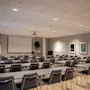 Et konferanserom er satt opp med rader av tomme stoler vendt mot en stor projeksjonsskjerm. Veggene er dekorert med innrammet kunst, noe som skaper et profesjonelt og organisert miljø.