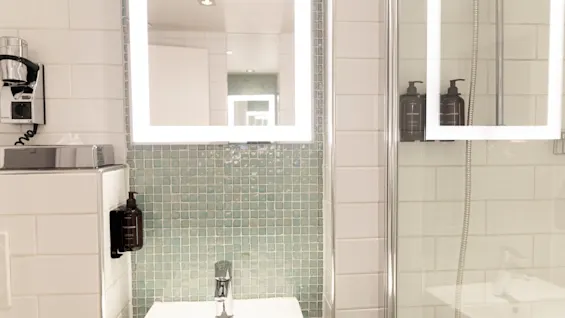 A modern bathroom at Home Hotel Grand Bodø with a lighted mirror, sink, and shower, equipped for personal care.