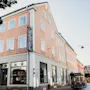 Persikanvärinen hotellirakennus, jonka kulmassa on näkyvä pystysuora HOTEL-kyltti, sijaitsee aurinkoisella kadulla muiden rakennusten ja pysäköityjen polkupyörien kanssa.
