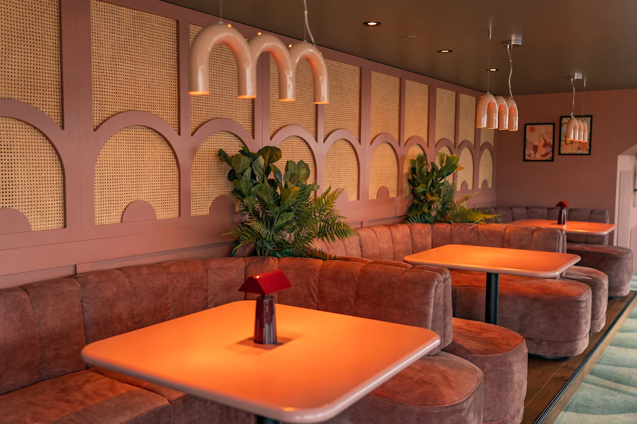 Eloisa ja kutsuva ravintolan sisustus, jossa on mukavat loosipaikat, lämpimän oranssit pöydät ja tyylikkäät rottinkiseinäkoristeet.