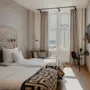 Valoisa hotellihuone, jossa kaksi erillistä sänkyä, kuvioitu sängynpääty, ikkuna näköalalla ja pieni työpöytäalue.
