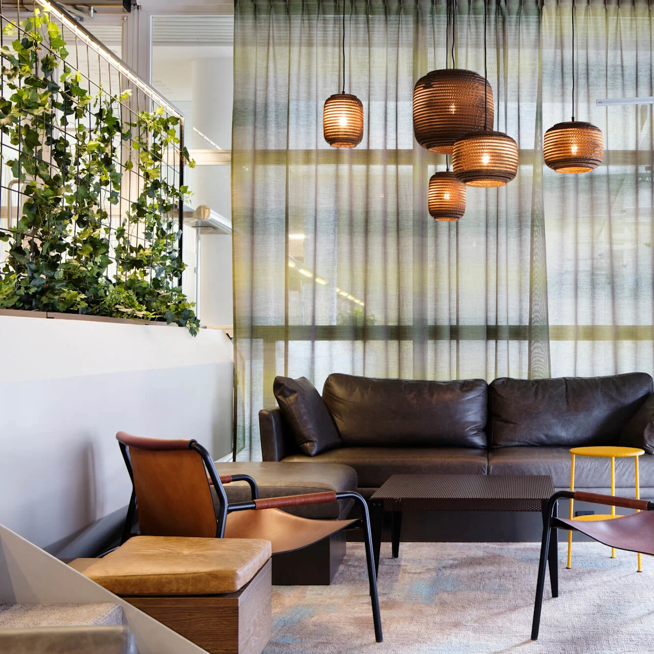 En moderne lounge med lædersæder og hængende kobberlamper, mod en baggrund af gennemsigtige gardiner og stueplanter.