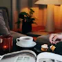 En person som koser seg med kaffe og kake i en koselig stue med tent lys.