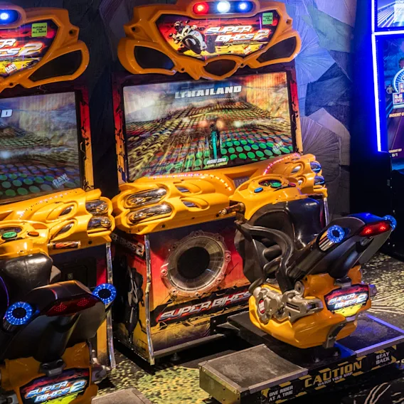 Två färgglada arkadmotorcykelracingspel med skärmar som visar en racerbana, redo för spelare.