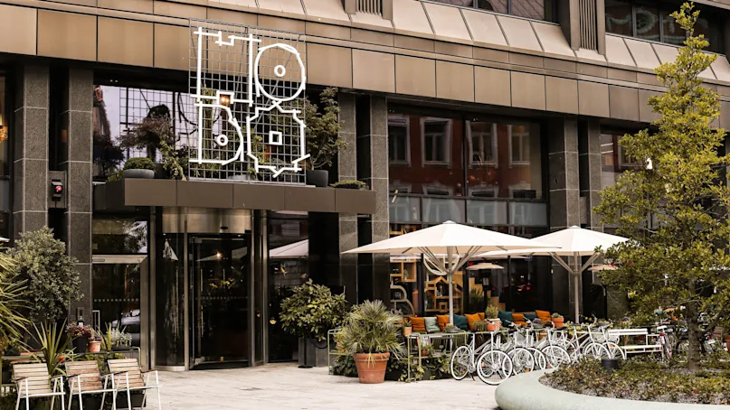 Hotel facade displays geometric Hobo signage above entrance, with potted plants and outdoor seating under umbrellas on a city street.